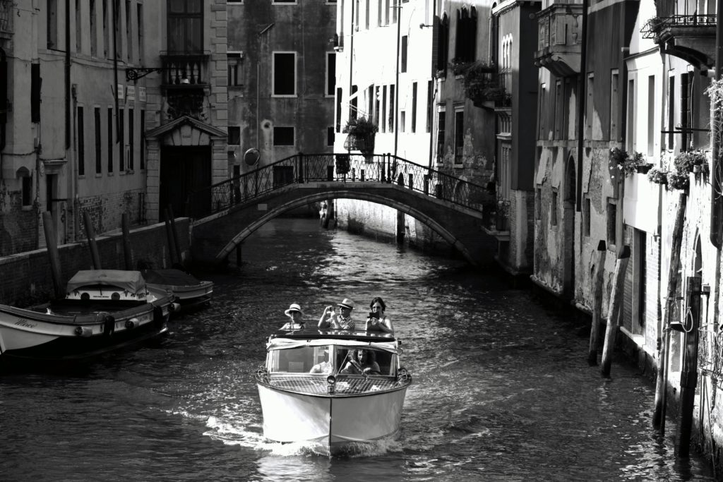 Grayscale photo of people riding a boat on canal in venice italy