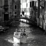 Grayscale photo of people riding a boat on canal in venice italy
